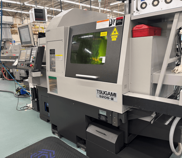Tsugami S205-II CNC Swiss lathe operating in a manufacturing facility with control panel and enclosed machining area visible